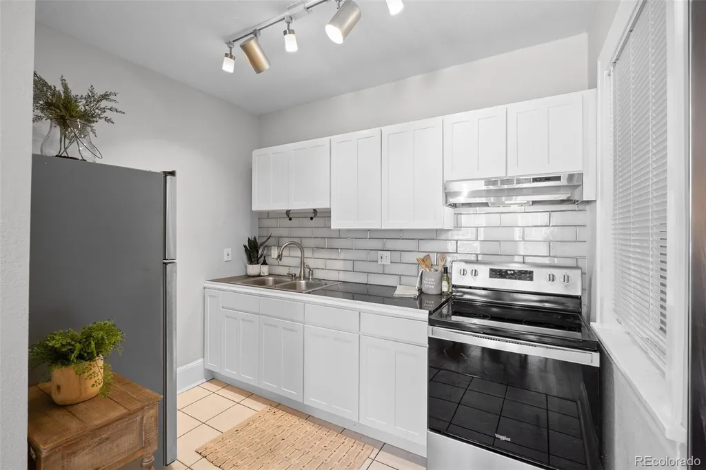 Kitchen with white cabinets, subway tile, stainless refrigerator and black range.