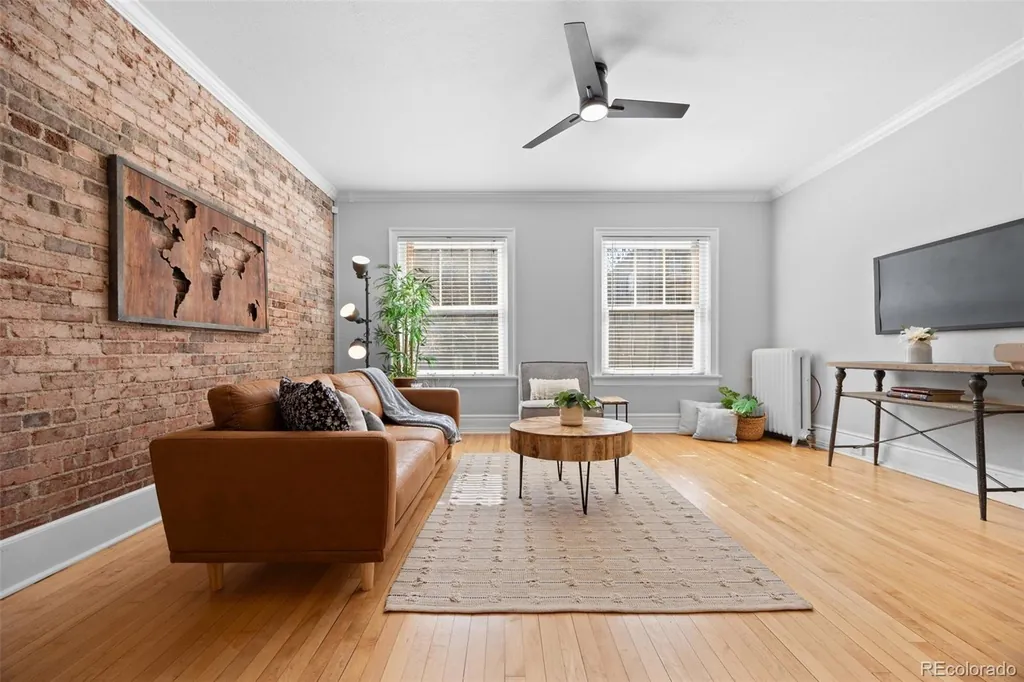Living room with an original exposed brick wall on the left, hardwood floors and two tall windows ahead